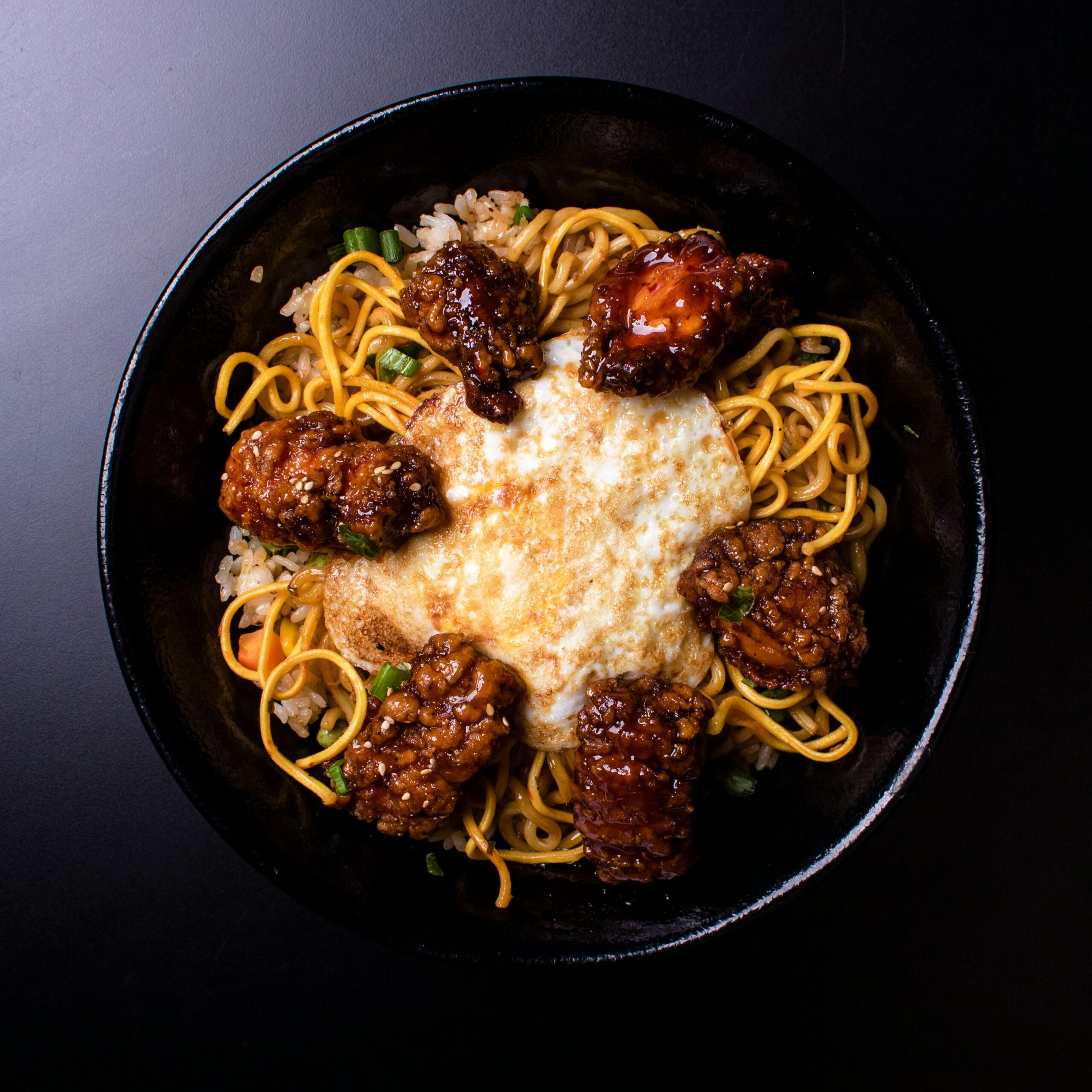 A delicious close-up of fried egg on noodles with spicy chicken in a dark setting.
